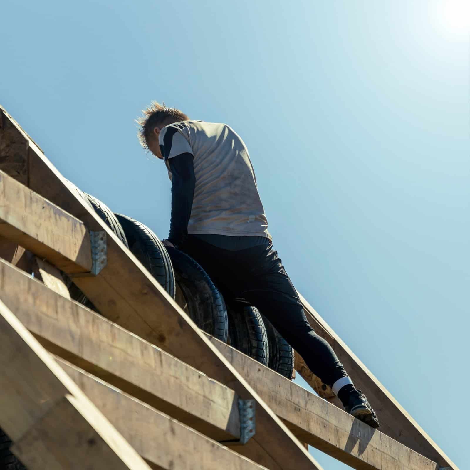 Roofing worker handling tires on wooden roof structure for roofing installation.